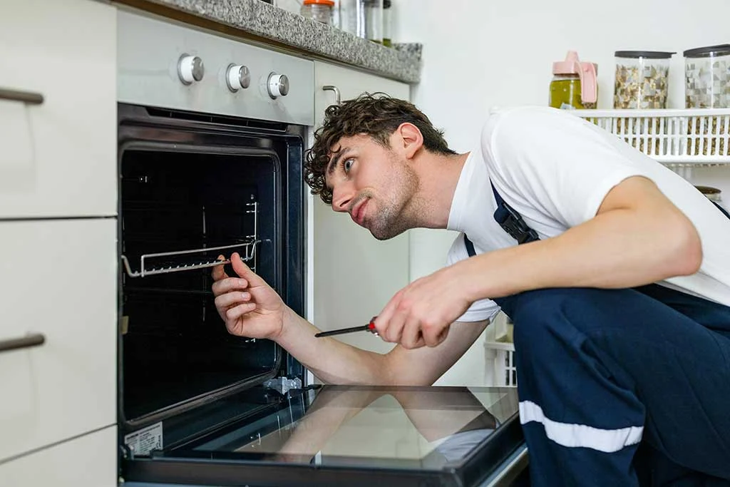 Appliance technician inspecting an open built-in oven in a home kitchen