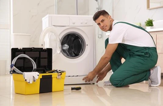 Technician in green overalls working beside a washing machine